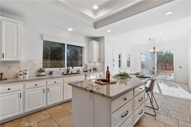 kitchen with a notable chandelier, a kitchen island, sink, white cabinetry, and hanging light fixtures