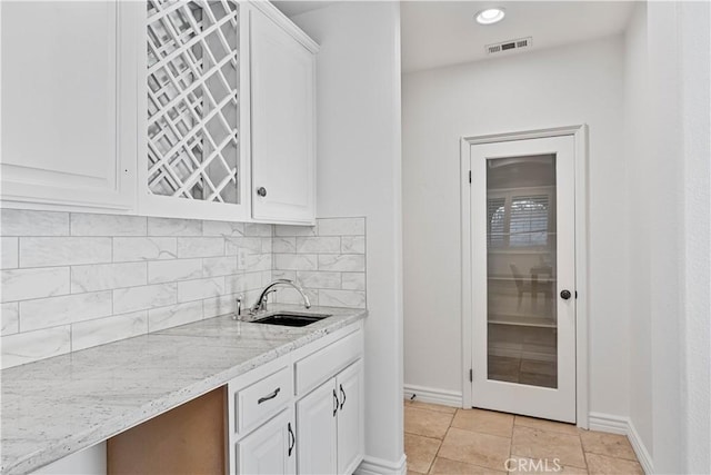 kitchen featuring light stone countertops, backsplash, white cabinets, and sink