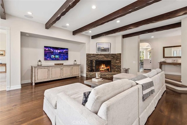 living room featuring dark hardwood / wood-style flooring, beamed ceiling, and a stone fireplace