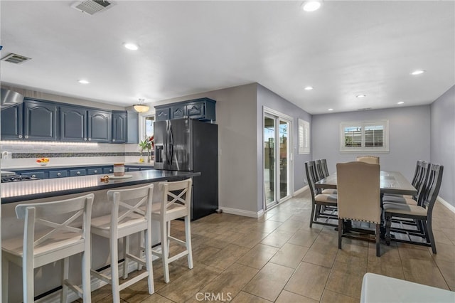 kitchen featuring a breakfast bar area, decorative backsplash, stainless steel gas cooktop, blue cabinets, and fridge with ice dispenser