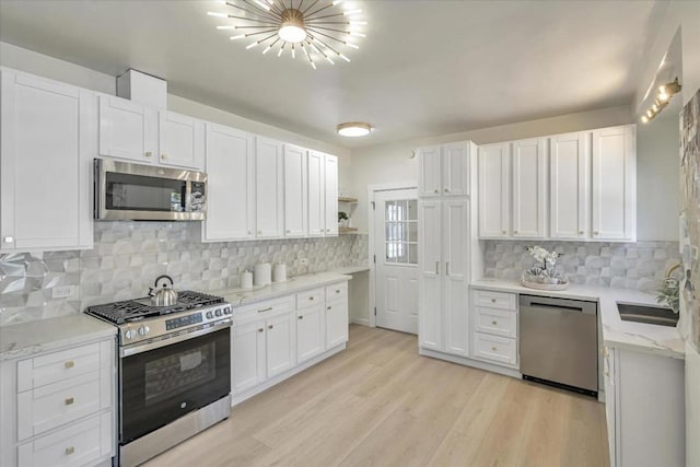 kitchen with light wood-type flooring, appliances with stainless steel finishes, decorative backsplash, and white cabinets