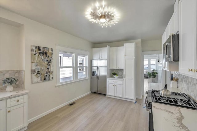 kitchen with tasteful backsplash, light stone countertops, stainless steel appliances, and white cabinetry