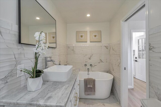 bathroom with a bathtub, vanity, and tile walls