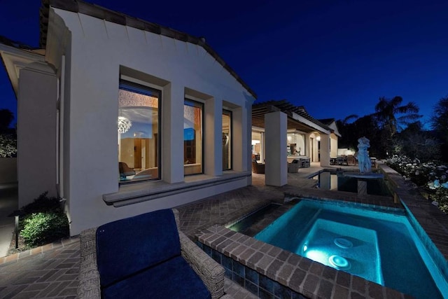 pool at night with an in ground hot tub and a patio area