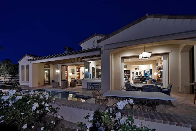 back house at night featuring a patio area and exterior bar