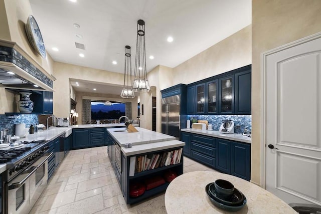 kitchen featuring high end appliances, backsplash, hanging light fixtures, a center island with sink, and blue cabinets