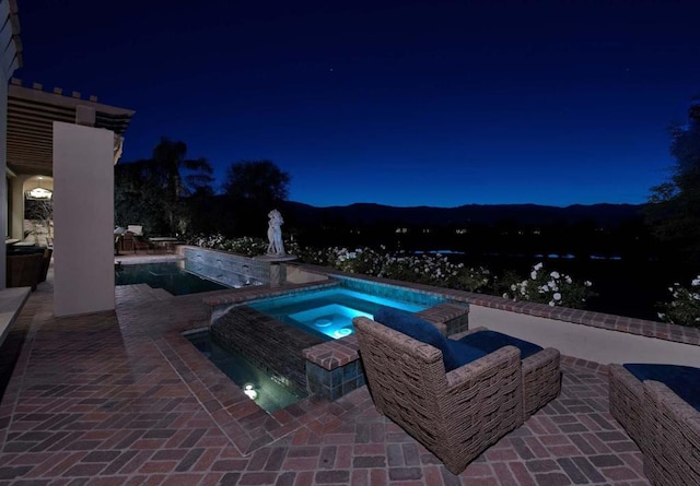 pool at twilight featuring an in ground hot tub and a patio area