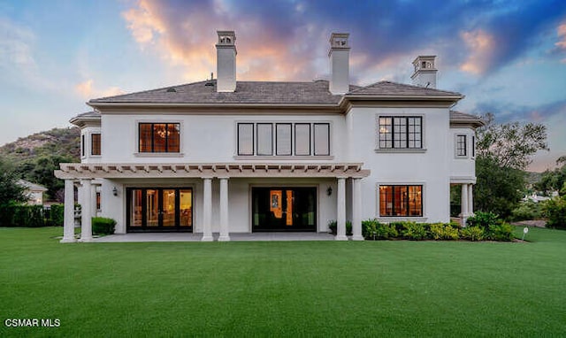 back house at dusk featuring a patio area and a yard