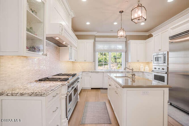 kitchen featuring decorative light fixtures, white cabinetry, a kitchen island with sink, and built in appliances