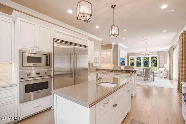 kitchen featuring an island with sink, sink, built in appliances, and pendant lighting