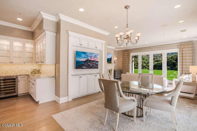 dining room featuring beverage cooler, french doors, ornamental molding, a notable chandelier, and light hardwood / wood-style flooring