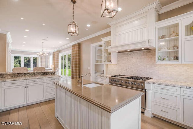 kitchen with stainless steel range, white cabinetry, hanging light fixtures, and an island with sink