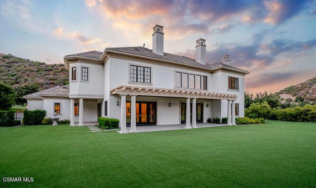 back house at dusk featuring a lawn and a patio