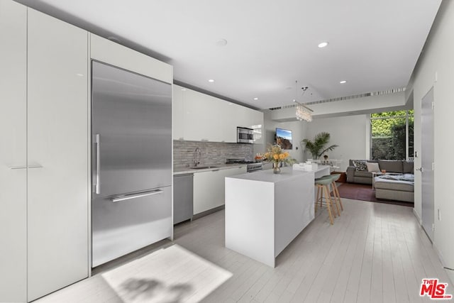 kitchen featuring appliances with stainless steel finishes, a kitchen island, pendant lighting, white cabinets, and a breakfast bar