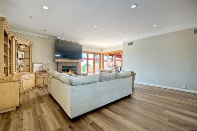 living room with light hardwood / wood-style floors, crown molding, and a tiled fireplace