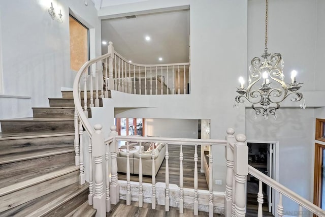 stairs featuring wood-type flooring, a notable chandelier, and a high ceiling