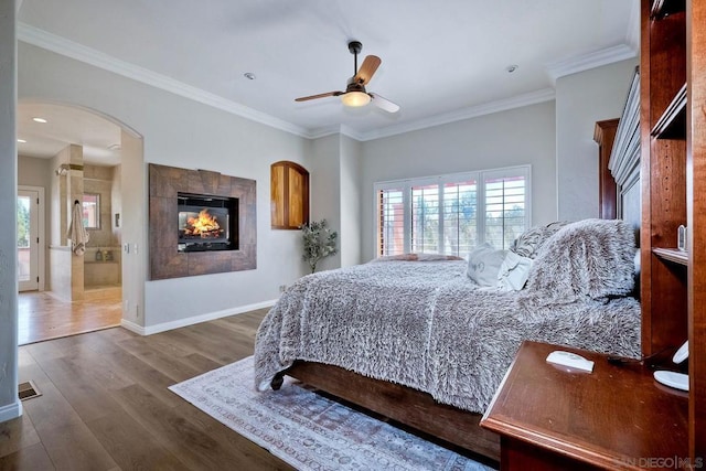 bedroom with connected bathroom, dark hardwood / wood-style flooring, a fireplace, ceiling fan, and crown molding