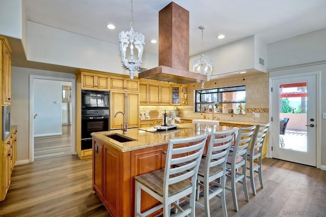 kitchen with black appliances, decorative backsplash, a kitchen bar, island exhaust hood, and a kitchen island with sink