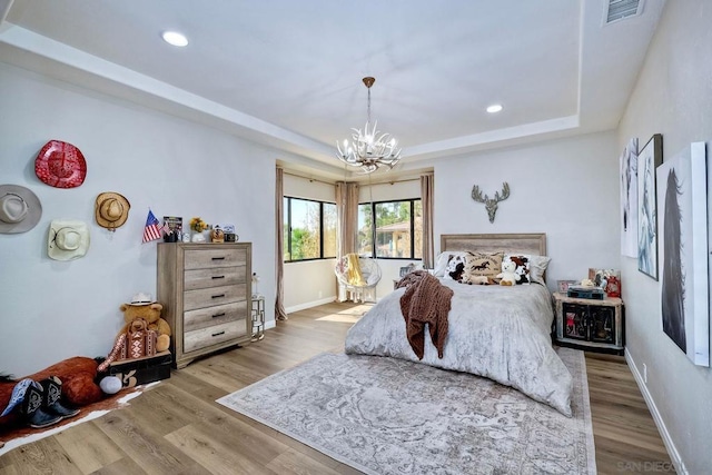 bedroom with wood-type flooring, a raised ceiling, and a notable chandelier