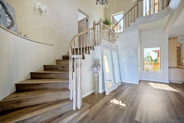 stairway featuring a towering ceiling, hardwood / wood-style flooring, and a notable chandelier