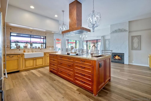 kitchen featuring a tiled fireplace, sink, a kitchen island with sink, and exhaust hood