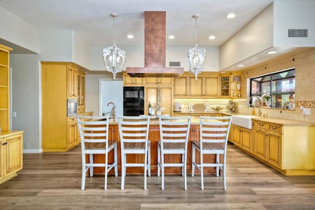 kitchen featuring decorative backsplash, black appliances, hanging light fixtures, and a kitchen island with sink