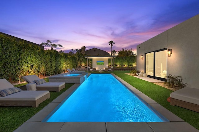 pool at dusk with an in ground hot tub and a yard