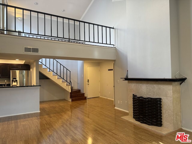 unfurnished living room with a tiled fireplace, hardwood / wood-style floors, and a high ceiling