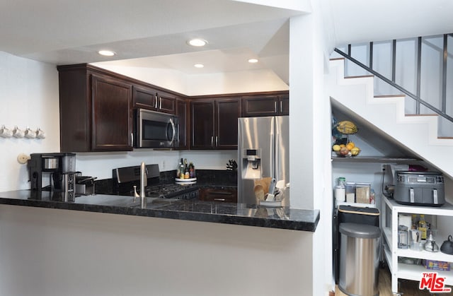 kitchen with dark brown cabinetry, sink, dark stone countertops, appliances with stainless steel finishes, and kitchen peninsula