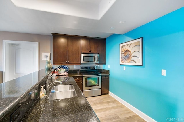 kitchen featuring stainless steel appliances, light wood-type flooring, dark stone countertops, dark brown cabinets, and sink