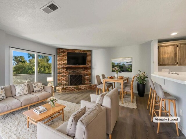 living room featuring a brick fireplace, a textured ceiling, and dark hardwood / wood-style floors