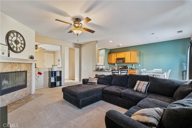 living room featuring ceiling fan, light colored carpet, and a tiled fireplace