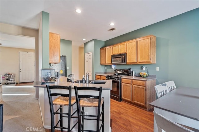 kitchen with black appliances, sink, light hardwood / wood-style flooring, a kitchen breakfast bar, and light brown cabinets