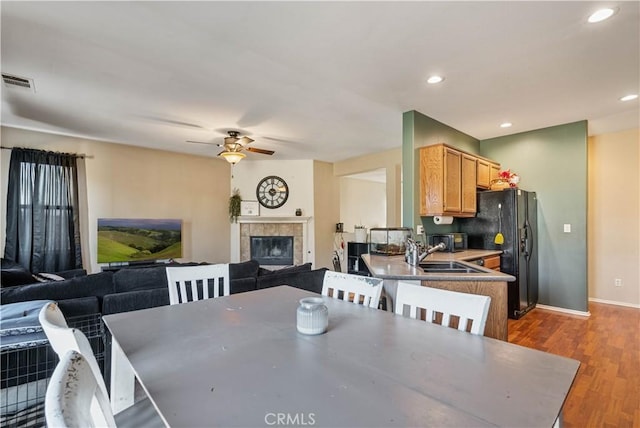 dining room with ceiling fan, a tiled fireplace, sink, and light hardwood / wood-style flooring