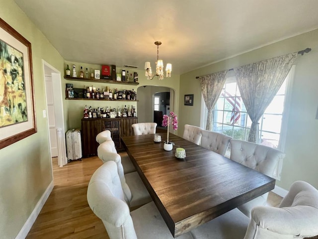 dining space with an inviting chandelier, indoor bar, and light wood-type flooring