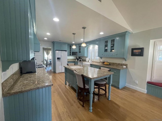 kitchen with a wealth of natural light, pendant lighting, white fridge with ice dispenser, blue cabinetry, and light wood-type flooring