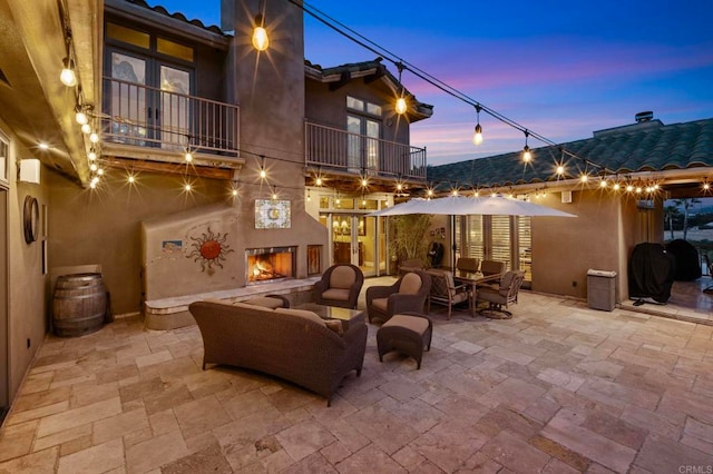 patio terrace at dusk featuring a balcony, a grill, and an outdoor living space with a fireplace