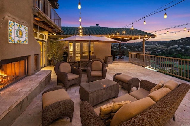 patio terrace at dusk featuring a balcony and an outdoor living space with a fireplace