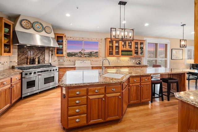 kitchen with double oven range, an island with sink, backsplash, decorative light fixtures, and sink