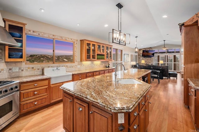 kitchen with sink, stainless steel stove, lofted ceiling, and an island with sink