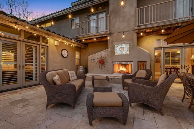 patio terrace at dusk with french doors, an outdoor living space with a fireplace, and a balcony