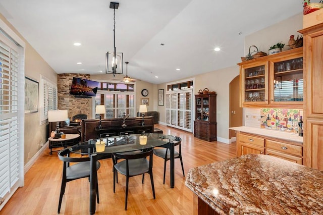 dining room featuring light hardwood / wood-style floors, vaulted ceiling, ceiling fan, and a fireplace