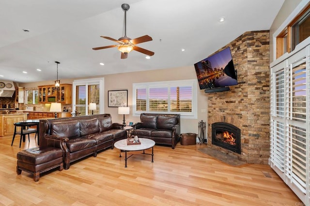 living room featuring ceiling fan, light hardwood / wood-style flooring, and a stone fireplace