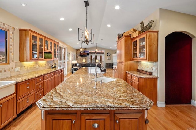 kitchen featuring decorative light fixtures, decorative backsplash, sink, vaulted ceiling, and a center island with sink