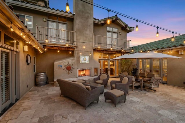 patio terrace at dusk with an outdoor living space with a fireplace and a balcony