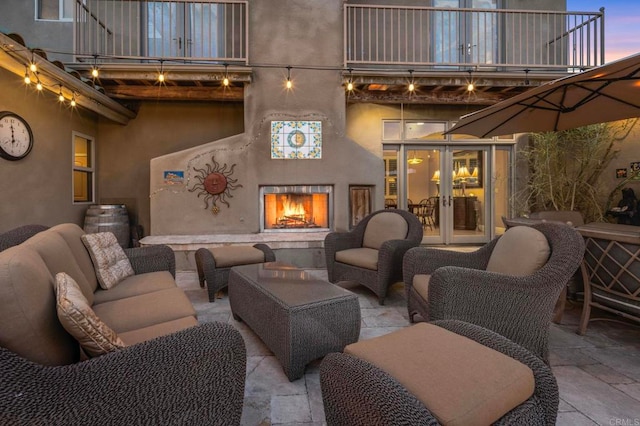 patio terrace at dusk with a balcony, an outdoor living space, and french doors