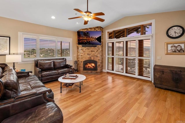 living room featuring lofted ceiling, light wood-type flooring, a brick fireplace, and ceiling fan