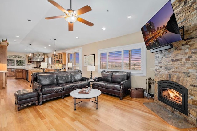 living room with sink, a large fireplace, vaulted ceiling, ceiling fan, and light hardwood / wood-style flooring