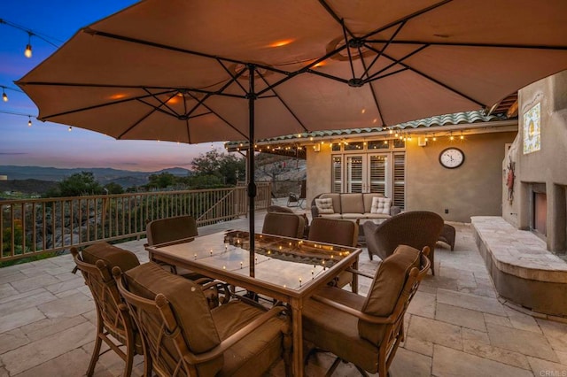 patio terrace at dusk with an outdoor living space with a fireplace and a mountain view