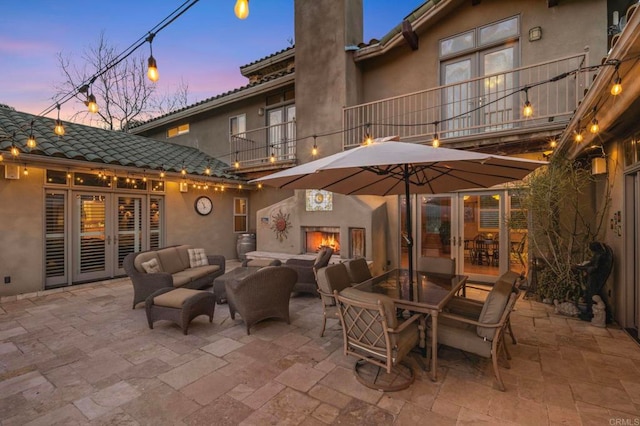 patio terrace at dusk featuring an outdoor living space with a fireplace and a balcony